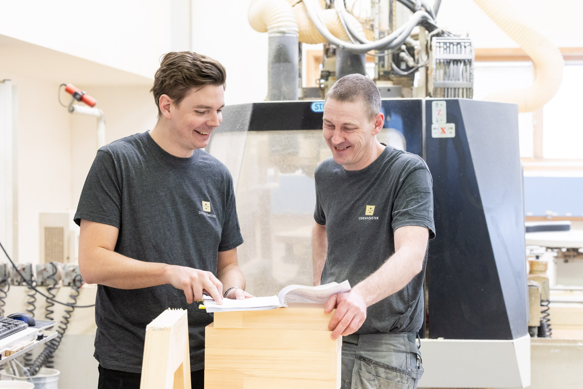 Två män som diskuterar fönsterritningar framför CNC